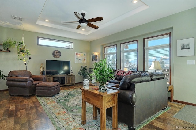 living room with dark hardwood / wood-style flooring, ceiling fan, and a raised ceiling