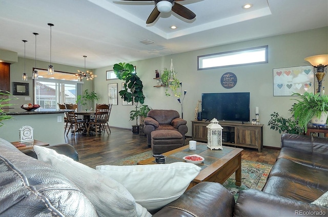 living room with a raised ceiling, dark hardwood / wood-style floors, and ceiling fan with notable chandelier