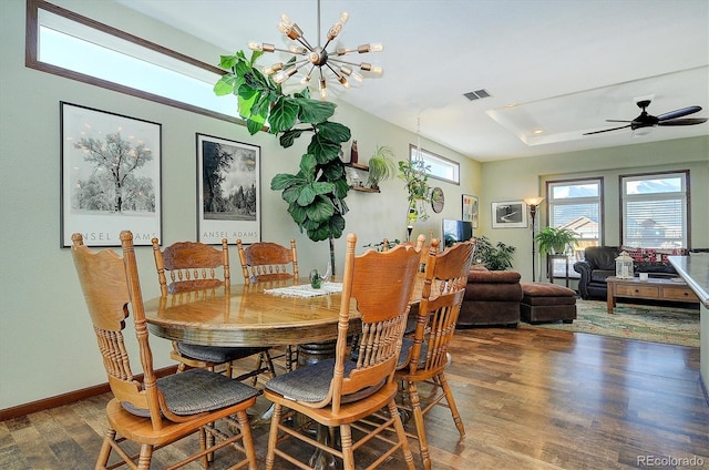 dining space featuring a raised ceiling, ceiling fan with notable chandelier, and dark hardwood / wood-style flooring