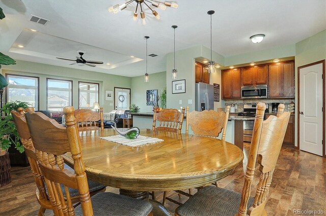 dining space with a tray ceiling, ceiling fan with notable chandelier, and dark hardwood / wood-style floors