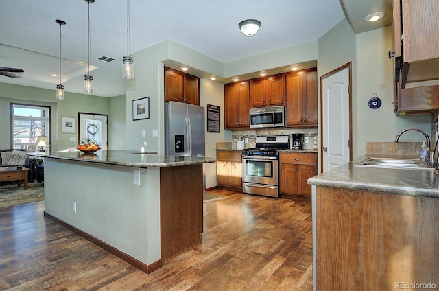 kitchen featuring dark wood-type flooring, sink, decorative backsplash, decorative light fixtures, and stainless steel appliances