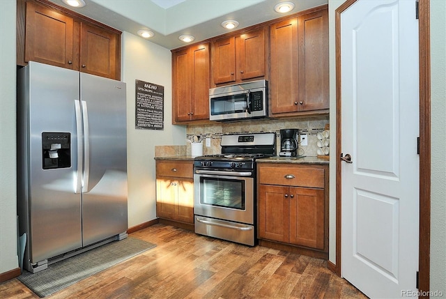 kitchen with dark stone countertops, decorative backsplash, light hardwood / wood-style flooring, and appliances with stainless steel finishes