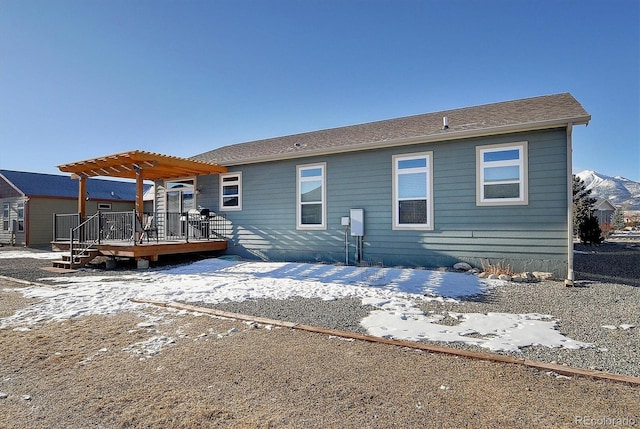 snow covered back of property with a pergola and a wooden deck