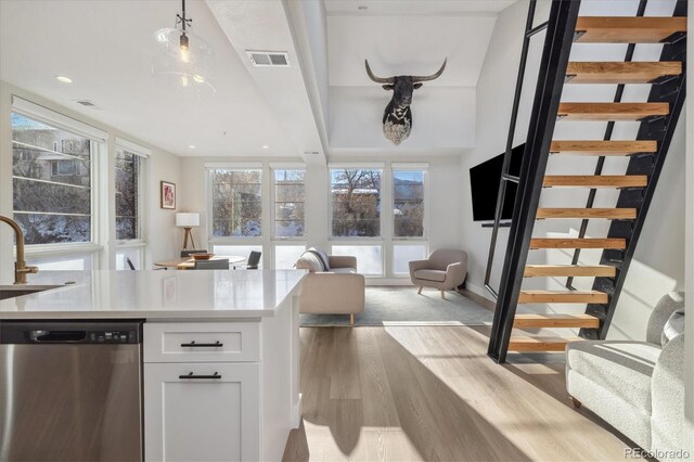 kitchen featuring sink, white cabinets, hanging light fixtures, stainless steel dishwasher, and light wood-type flooring