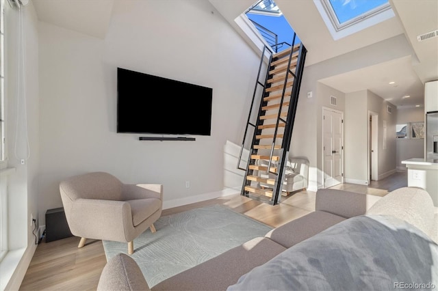 living room with a skylight, high vaulted ceiling, and light hardwood / wood-style flooring