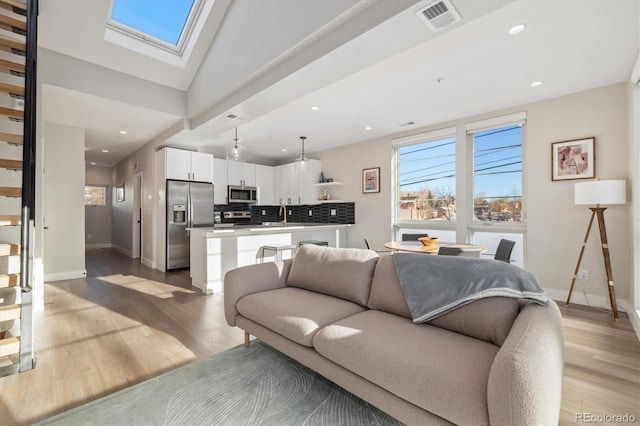 living room with sink, a skylight, and light hardwood / wood-style floors