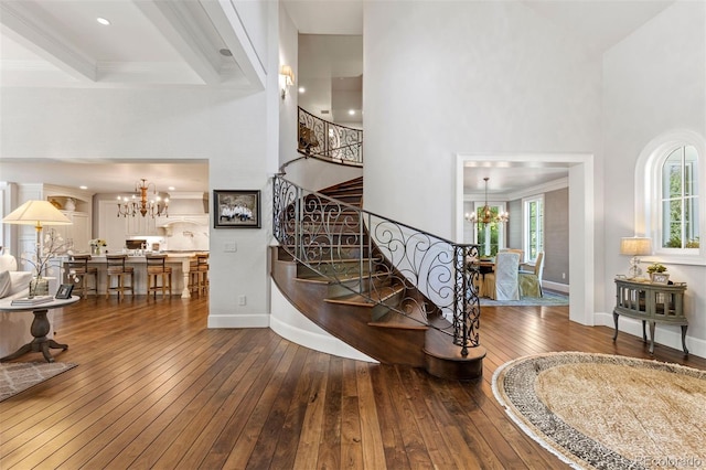 stairs with a notable chandelier, baseboards, a towering ceiling, and hardwood / wood-style floors