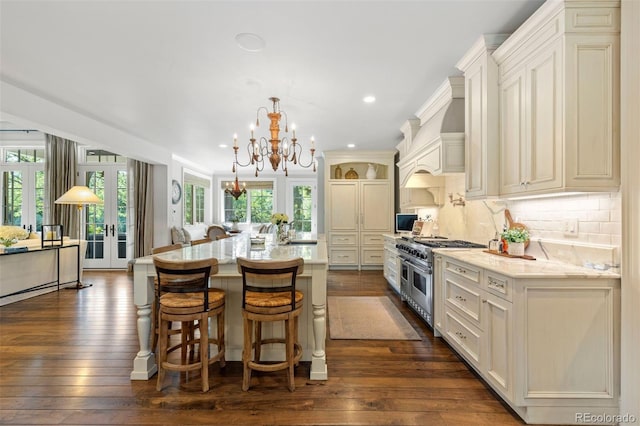 kitchen featuring tasteful backsplash, dark wood finished floors, range with two ovens, french doors, and a notable chandelier