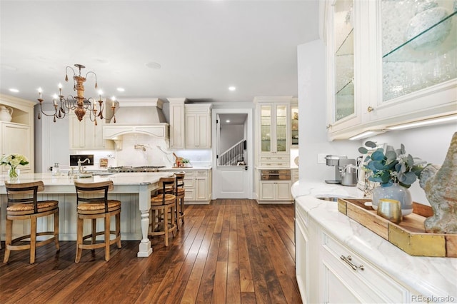 kitchen featuring custom exhaust hood, white cabinets, light stone counters, and glass insert cabinets