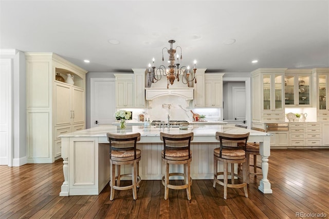 kitchen with a large island, dark wood-type flooring, light stone counters, an inviting chandelier, and decorative backsplash