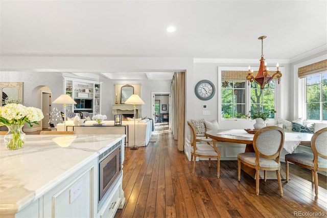 kitchen featuring stainless steel microwave, dark wood-style floors, breakfast area, light stone countertops, and a chandelier