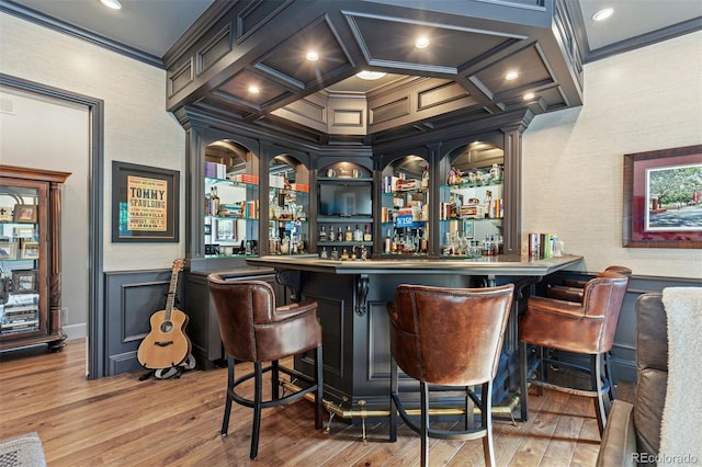 bar with a dry bar, ornamental molding, wood finished floors, a decorative wall, and coffered ceiling