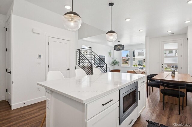 12270 W 57th Ave, Arvada, CO 80002 - kitchen with stainless steel microwave, dark wood-style flooring, a center island, white cabinetry, and decorative light fixtures