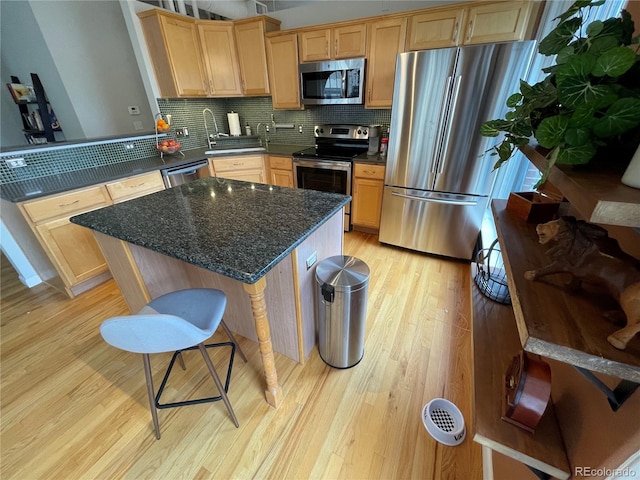 kitchen featuring a breakfast bar area, appliances with stainless steel finishes, a center island, tasteful backsplash, and light hardwood / wood-style floors