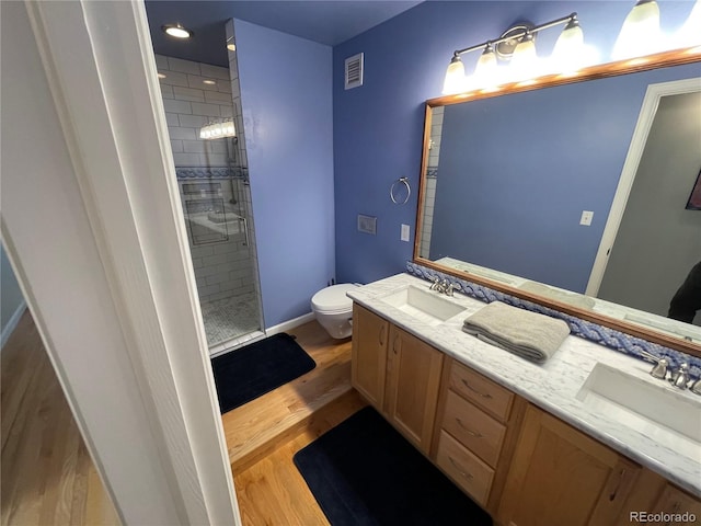 bathroom featuring hardwood / wood-style flooring, tiled shower, vanity, and toilet