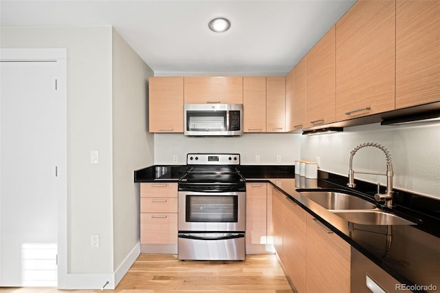 kitchen with stainless steel appliances, sink, light brown cabinetry, and light hardwood / wood-style floors