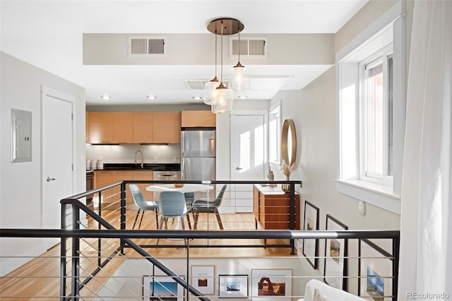 kitchen featuring sink, light brown cabinets, stainless steel refrigerator, electric panel, and pendant lighting