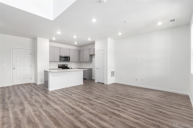 kitchen with stainless steel appliances, gray cabinetry, light wood-style flooring, open floor plan, and recessed lighting