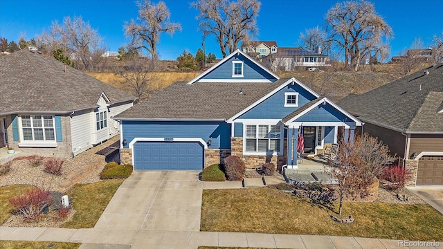 craftsman-style home with a garage, concrete driveway, a shingled roof, and stone siding