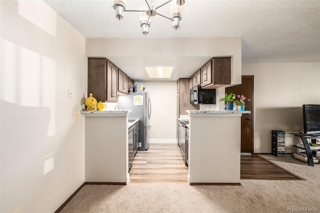 kitchen with appliances with stainless steel finishes, a notable chandelier, light colored carpet, and a textured ceiling