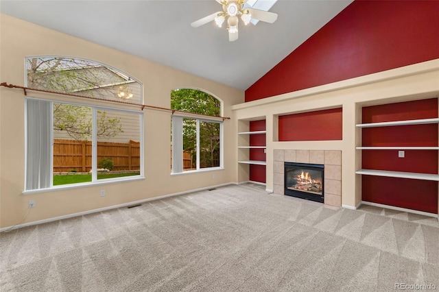 3371 Bexley Dr, Colorado Springs, CO 80922 - unfurnished living room with high vaulted ceiling, carpet flooring, ceiling fan, a tiled fireplace, and built in shelves