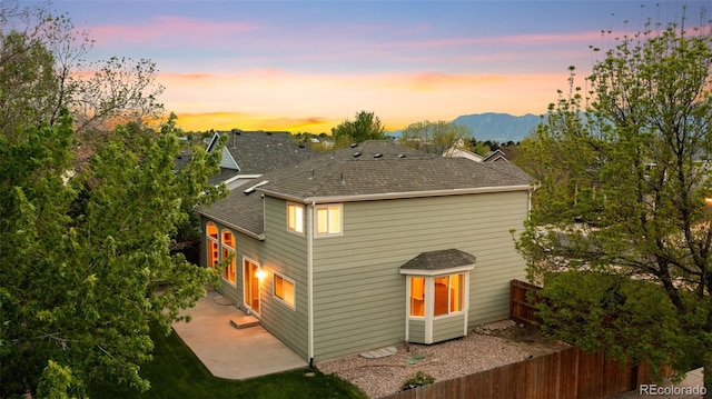 3371 Bexley Dr, Colorado Springs, CO 80922 - back of property at dusk featuring a patio, a shingled roof, fence, and a mountain view