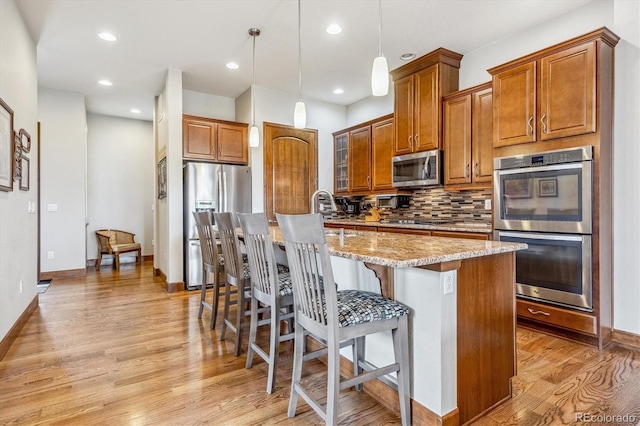 kitchen with appliances with stainless steel finishes, light hardwood / wood-style floors, a kitchen island with sink, and backsplash