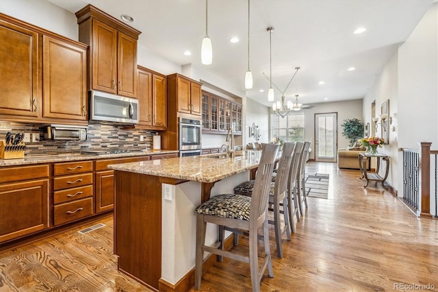 kitchen featuring appliances with stainless steel finishes, backsplash, light hardwood / wood-style floors, a kitchen island with sink, and a breakfast bar