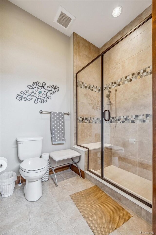 bathroom featuring toilet, a shower with door, and tile patterned floors