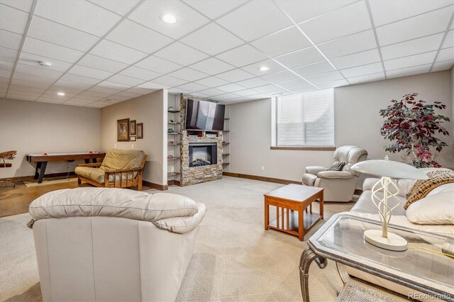 carpeted living room featuring a stone fireplace and a paneled ceiling