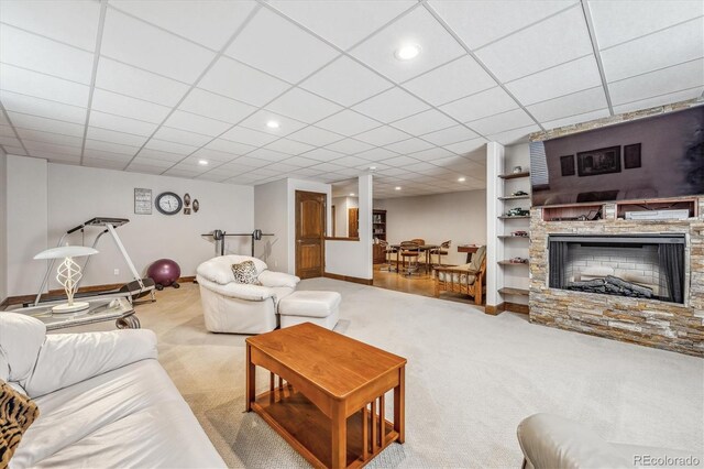 carpeted living room with a paneled ceiling, a stone fireplace, and built in shelves