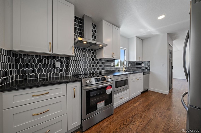 kitchen with wall chimney exhaust hood, stainless steel appliances, dark countertops, a sink, and dark wood-type flooring