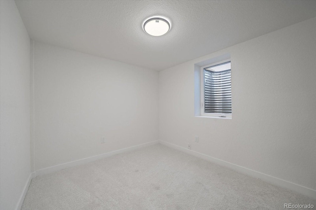 empty room with light colored carpet, baseboards, and a textured ceiling