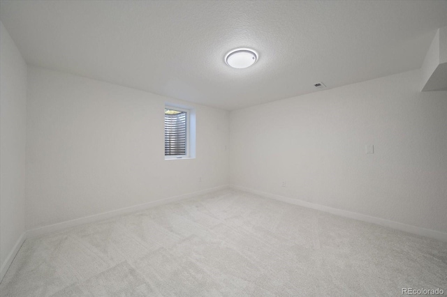spare room with light colored carpet, baseboards, and a textured ceiling