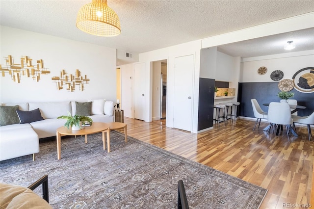 living area with visible vents, a textured ceiling, and wood finished floors