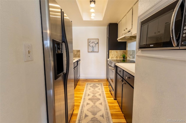 kitchen featuring under cabinet range hood, stainless steel appliances, light wood finished floors, a raised ceiling, and light countertops