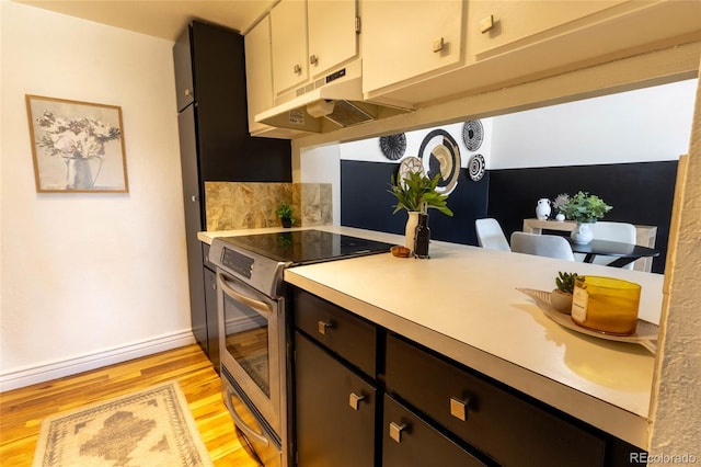 kitchen featuring baseboards, under cabinet range hood, light countertops, stainless steel range with electric stovetop, and light wood-style floors