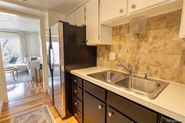 kitchen with backsplash, light wood-type flooring, light countertops, white cabinets, and a sink