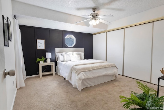 bedroom featuring a closet, light carpet, a textured ceiling, and ceiling fan