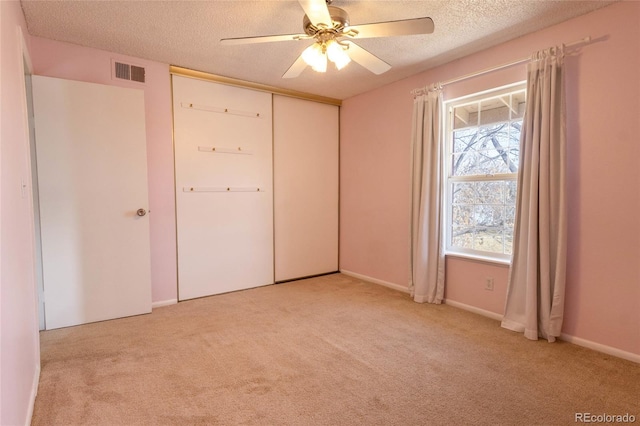 unfurnished bedroom featuring ceiling fan, light colored carpet, visible vents, and a textured ceiling