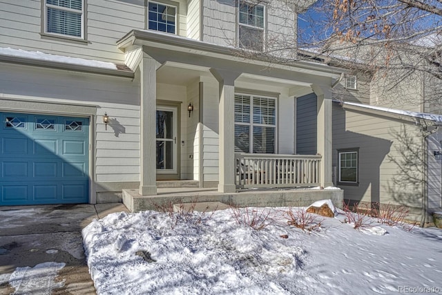 snow covered property entrance featuring a porch and a garage