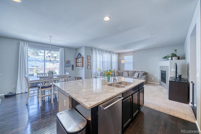 kitchen featuring sink, stainless steel dishwasher, a textured ceiling, decorative light fixtures, and a center island with sink