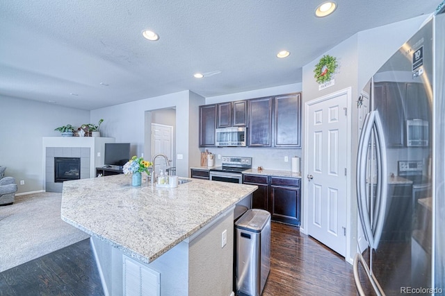 kitchen featuring a kitchen breakfast bar, a textured ceiling, stainless steel appliances, sink, and an island with sink