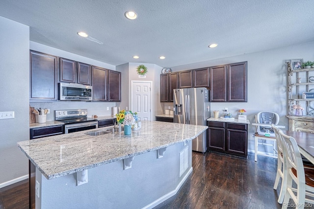 kitchen featuring a center island with sink, a kitchen breakfast bar, sink, appliances with stainless steel finishes, and dark brown cabinetry