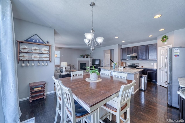 dining room with sink, dark wood-type flooring, an inviting chandelier, a textured ceiling, and a fireplace