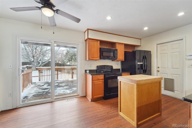 kitchen with hardwood / wood-style flooring, a kitchen island, ceiling fan, and black appliances