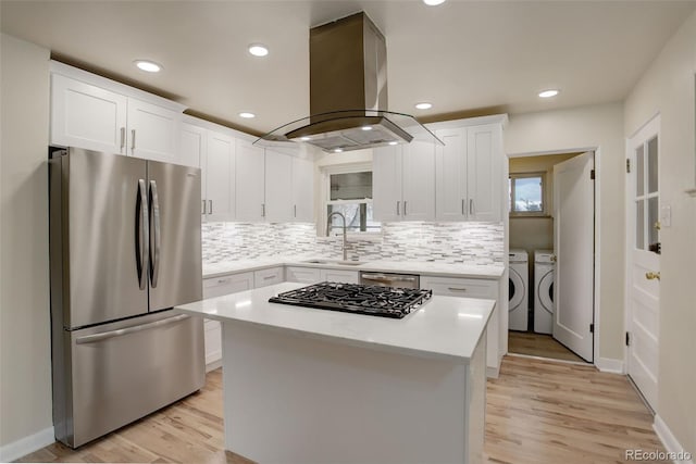 kitchen with a kitchen island, white cabinets, island exhaust hood, stainless steel appliances, and washer and clothes dryer