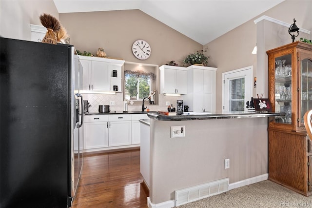 kitchen with lofted ceiling, dark countertops, visible vents, freestanding refrigerator, and white cabinets