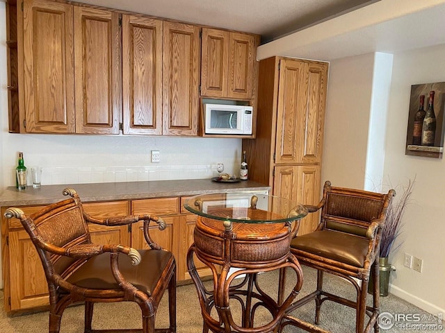 bar featuring a bar, white microwave, light carpet, and baseboards