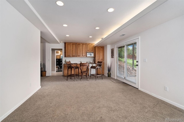 kitchen with a breakfast bar, white microwave, brown cabinets, and light colored carpet